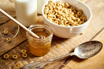 Healthy morning breakfast bowl full of honey flakes with honey dipper and milk on an old wooden table