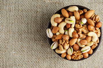 Mix of different nuts in a wooden cup against the background of fabric from burlap. Nuts as structure and background, macro. Top view.