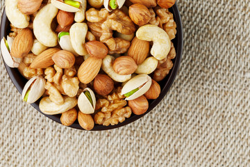 Mix of different nuts in a wooden cup against the background of fabric from burlap. Nuts as structure and background, macro. Top view.