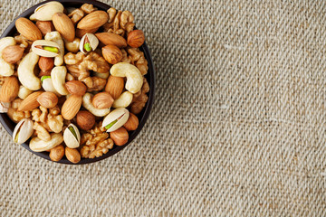 Mix of different nuts in a wooden cup against the background of fabric from burlap. Nuts as structure and background, macro. Top view.