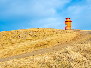 Stykkisholmur lighthouse on hill with yellow meadow under cloudy blue sky in Iceland