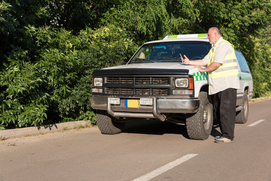 A mature man using his smartphone while standing next to his pickup truck in a sunny outdoor environment.