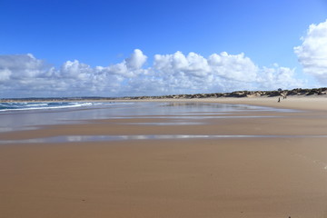 sand in the foreground with people in the background and sky with white clouds