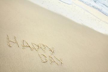 handwritten inscription happy day made in the sand near the water, the wave washes text on the beach
