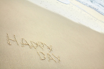 handwritten inscription happy day made in the sand near the water, the wave washes text on the beach
