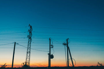 Power lines in field on sunrise background. Silhouettes of poles with wires at dawn. Cables of high...