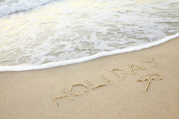 handwritten inscription holiday made in the sand near the water, the wave washes text on the beach
