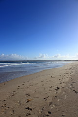 footprints in the sand of the beach with blue sky in the background