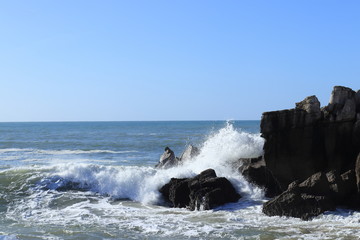 water to hit the rocks creating white foam and blue sky
