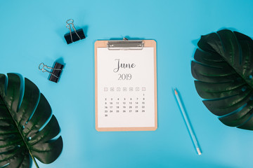Flat lay calendar with clipboard, palm leaves and pencil on blue background. June 2019. top view.