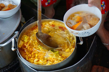 Delicious colorful soup stock with tomato slices pork potato tofu cabbage chilly sauce yellow color steamed meat stock for fish cake noodles Vietnamese traditional food Asian cuisine street food