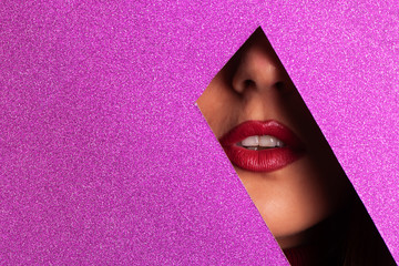 Girl with bright make up, red lipstick looking through hole in violet paper. Make up artist, beauty concept. Ready to party. Cosmetics sale. Beauty salon advertising banner with copy space