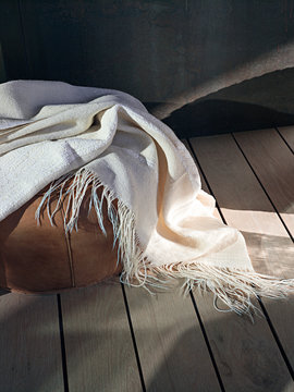 Plaid Tagesdecke Wolldecke auf Lederhocker Pouffe auf Holzboden vor Metallwand