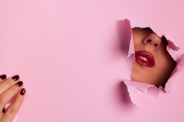 View of bright lips through hole in pink paper background. Make up artist, beauty concept. Ready to...