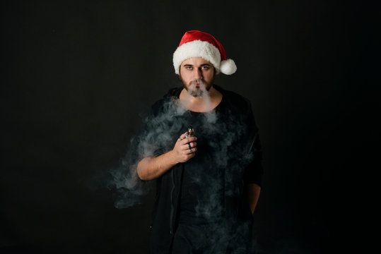 Man with beard in Santa red hat smoking electronic sigarette. vape pen. vape smoke. Christmas concept
