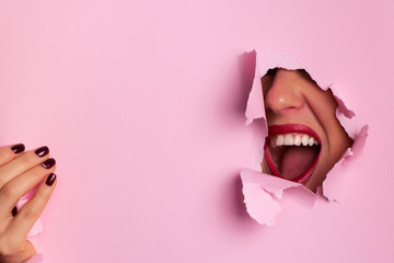 Screaming, hate, rage. Crying emotional angry woman screaming through hole in pink background. Emotional, young face. Human emotions, facial expression concept. Trendy colors