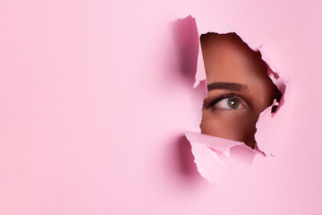 Girl with bright eyes make up looks through hole of pink paper. Business card of artist, beauty...
