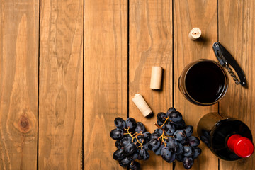 Wine bottle cups bunches of grapes and cork stopper on wooden background. Top view with copy space.