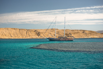 Obraz premium Sail boat in the coral sea near island. Summer vacation in an exotic country.