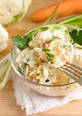 Sauerkraut salad with herbs in glass bowl is standing on table with fork and ingredients.
