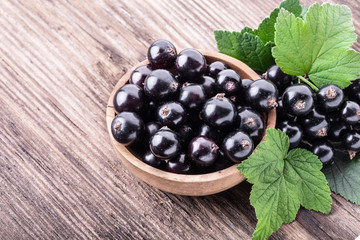 Fresh ripe black currant in wooden bowl with original leaves on rustic old background.