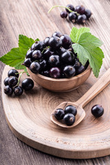 resh ripe black currant in wooden bowl with original leaves on rustic old background.