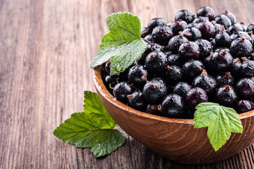 Big wooden bowl with fresh black currant and original leaves on wooden background.