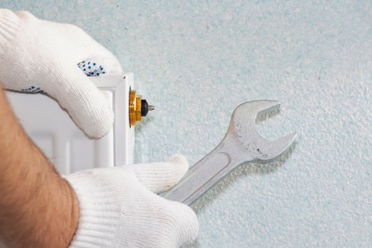 Man is repairing radiator battery in the room. Maintenance repair works renovation in the flat. Heating restoration. Wrench in hands