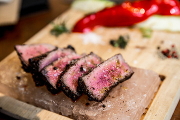 Juicy medium Beef Rib Eye steak slices in pan on Himalayan pink salt plates.