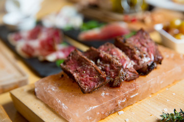 Juicy medium Beef Rib Eye steak slices in pan on Himalayan pink salt plates.
