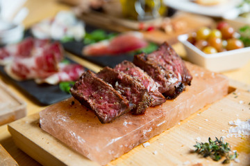 Juicy medium Beef Rib Eye steak slices in pan on Himalayan pink salt plates.