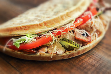 appetizing closed pizza calzone with pieces of meat, tomatoes, cheese, lettuce and pickles on a wooden background