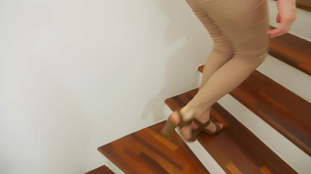 close-up, female legs in beige tight fitting pants and heeled sandals walking along a wooden modern staircase