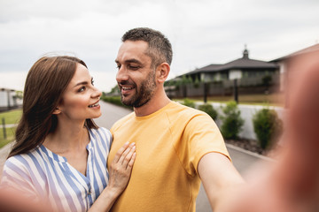 Obraz premium Hilarious hugging couple looking at each other with wide smile and making photo. Portrait. Street on blurred background