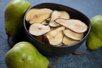 Pear fruit chips in a black bowl and fresh pears on a blue stone background, studio shot