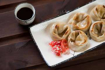 Pan fried asian dumplings with salmon, soy sauce and ginger. Rustic wooden background, close-up