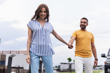 Happy woman holding male hand and looking at camera with smile. Man wearing yellow t-shirt locating...