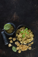 Bowl of orecchiette served with freshly made basil pesto sauce, flatlay with space on a dark brown stone background
