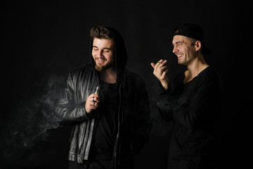 Bad habit, smoking in a public place. Two Young man blowing smoke to join it in one cloud at black...