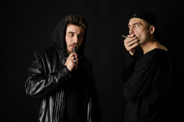 Bad habit, smoking in a public place. Two Young man blowing smoke to join it in one cloud at black...