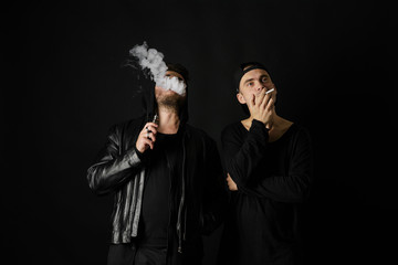 Bad habit, smoking in a public place. Two Young man blowing smoke to join it in one cloud at black...