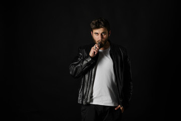 Man with vaping mod exhaling steam at black studio background. Bearded guy smoking e-cigarette to...