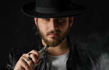 Man with vaping mod exhaling steam at black studio background. Bearded guy smoking e-cigarette to...