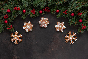Christmas holiday background with fir-tree branches with red berries and balls, with homemade snowflake shape gingerbread. Top view, close up dark concrete background.