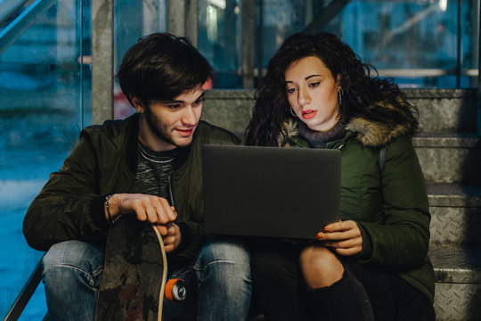 Couple of teenagers look at the laptop on a staircase outdoors