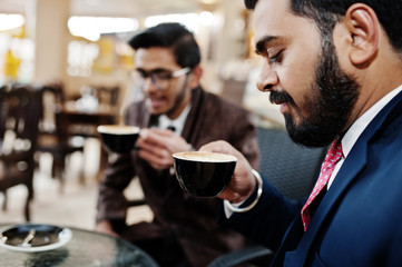 Two indian business man in suits sitting at office on cafe and drinking coffee.
