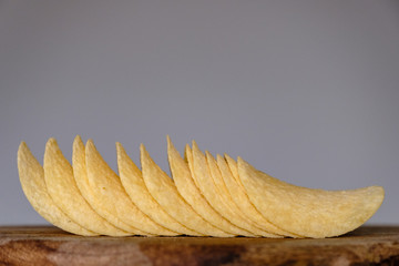 Bunch of salty crisps presented on a wooden board, grey background