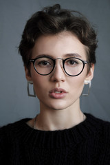 Fototapeta premium Young beautiful girl with short curly hair in glasses and black casual clothes, studio portrait.