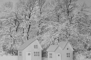 Small white cardboard houses, winter snowy trees background. Handmade home winter decoration. Do it yourself. Architecture business real estates concept. Shallow depth of focus. Black and white scene.