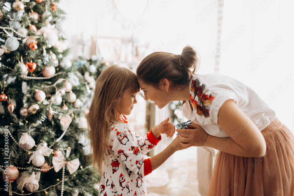 Wall mural gentle mother with her little daughter dressed in pajama next to the new year's tree in the full of 